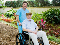 nurse pushing senior male in a wheelchair through a garden area