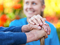image of a nurse with her hand on patient's hands while holding a walking cane