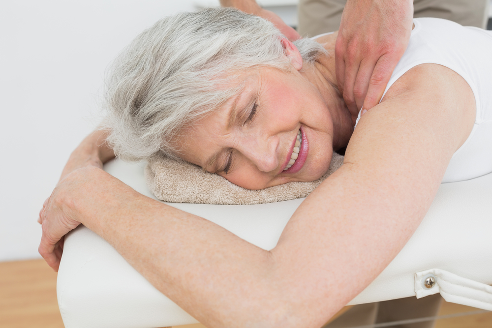 Male physiotherapist massaging a senior woman's shoulder in the medical office